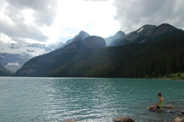 A girl looks out over Lake Louise with her feet in the cool water