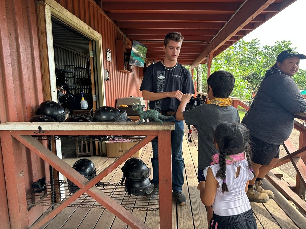 An employee at Kualoa Ranch handing kids their gear for the UTV tour.