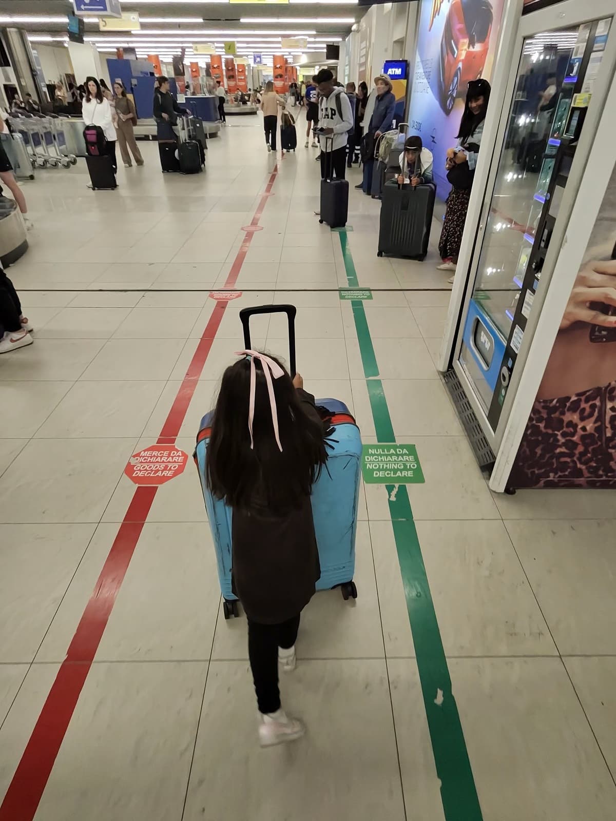 A little girl from behind walking through an airport with a large suitcase